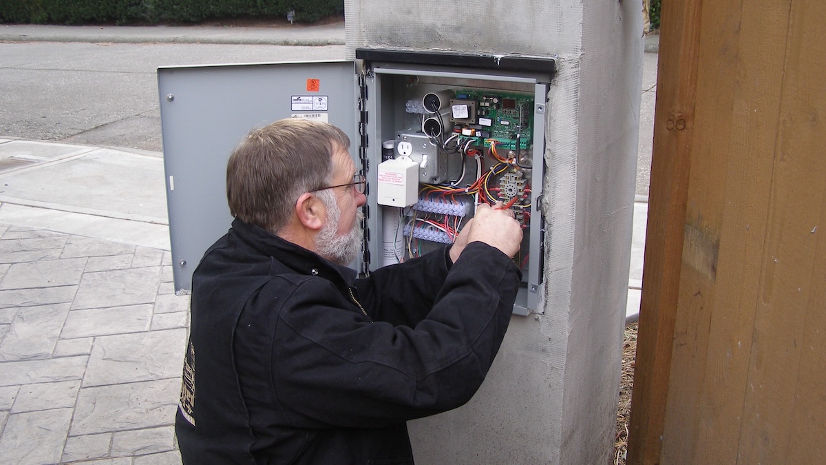 Gate Technician Inspects An Automated Gate Controller During A Maintenance Service Call
